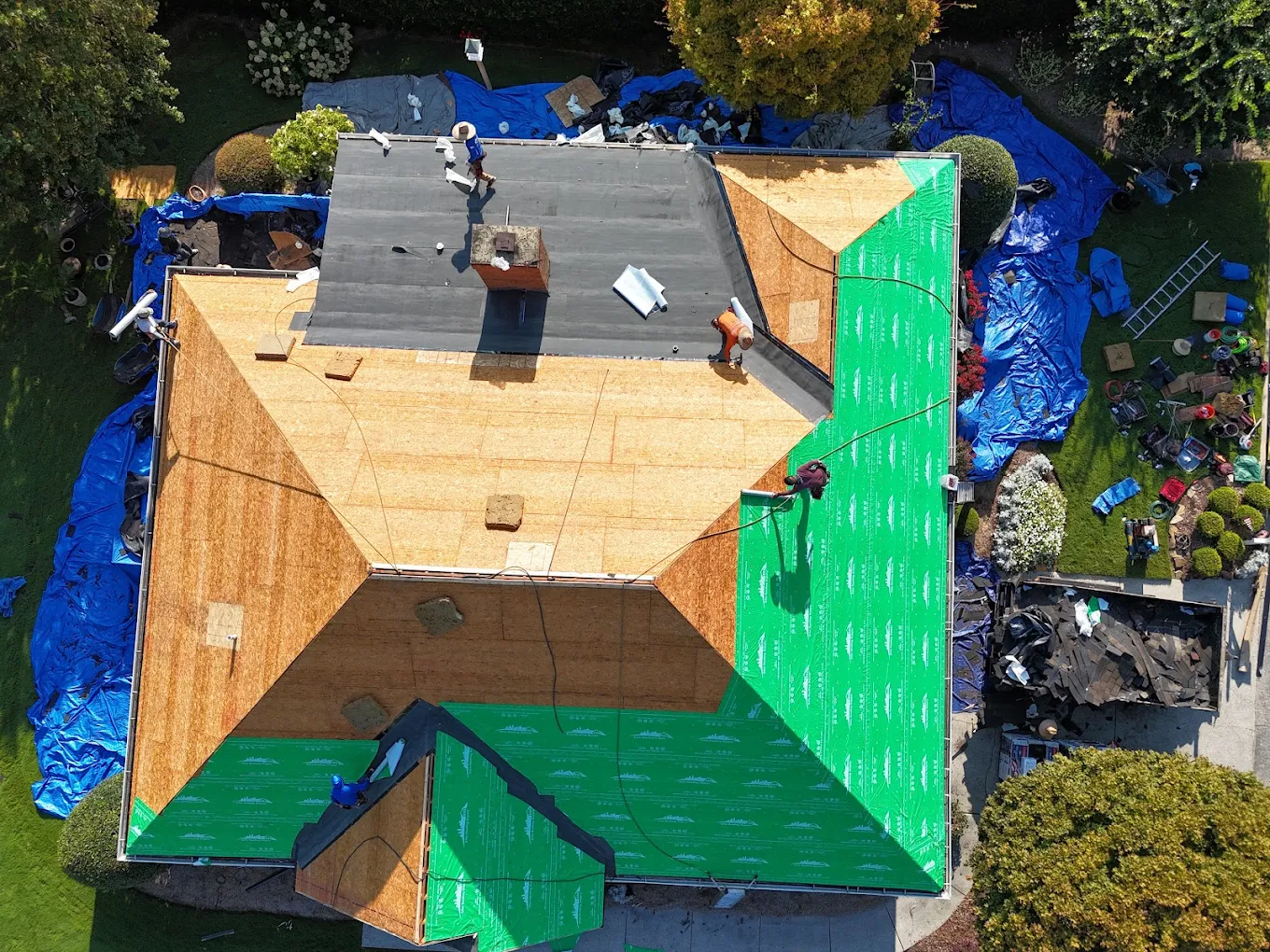 A North Georgia roof torn down to the decking after storm and hail damage, landscaping protected with tarps